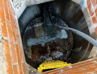 High-pressure jetting used to clean waste and residue from a manhole chamber.