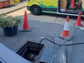 Safe manhole access setup with traffic management during drainage works.