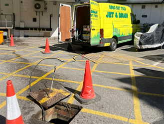Manhole chamber maintenance in progress with safety cones and warning barriers.