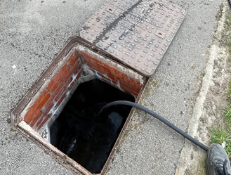Drain jetting hose inserted into manhole chamber for thorough cleaning.